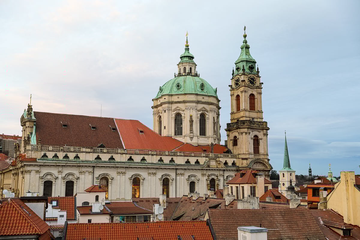 St. Nicholas Church in Prague’s Malá Strana district, with green copper dome and clock tower rising above the red rooftops of Lesser Town.