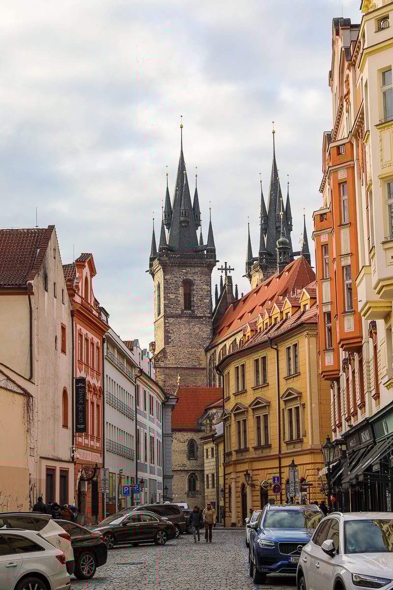 Street view of Old Town Prague with Gothic spires of the Church of Our Lady before Týn rising above pastel-colored buildings.