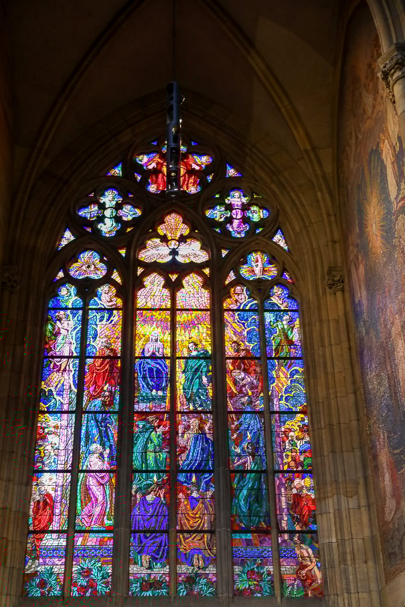 Colorful stained-glass window inside St. Vitus Cathedral in Prague, depicting biblical scenes and vibrant Gothic artistry.