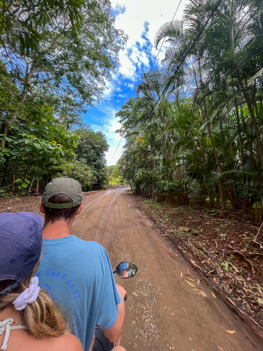 Maddy and Cacey riding a scooter on a dirt road in Costa Rica