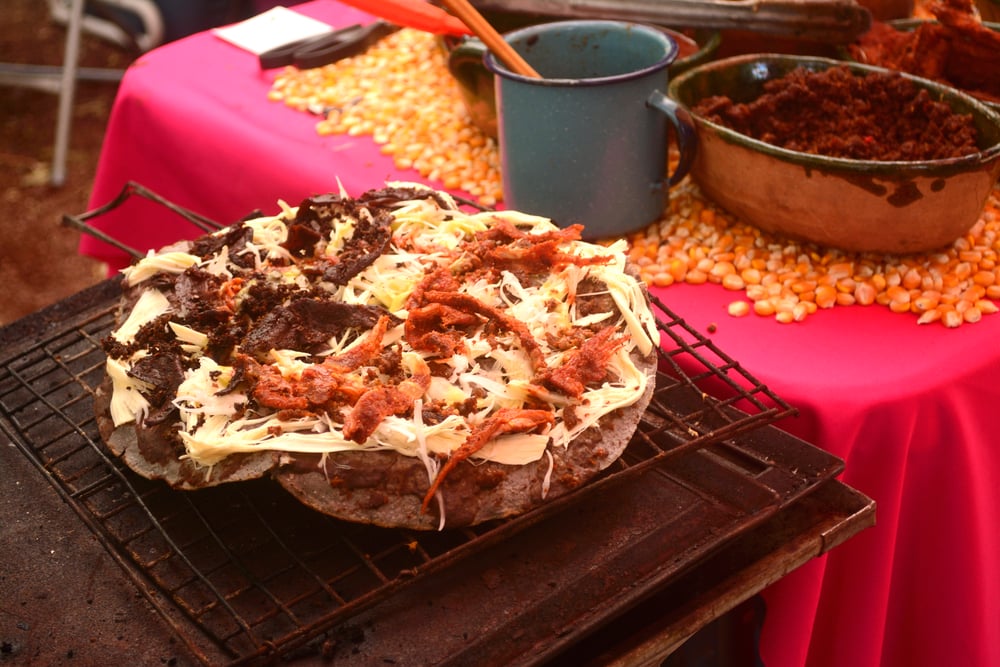 Tlayuda being cooked on an open fire with ingredients in the background