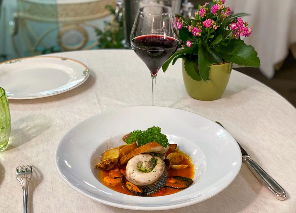 A plate of fresh seafood and a glass of wine on a white tablecloth. Eating as much seafood as possible is a must on any Amalfi Coast itinerary.