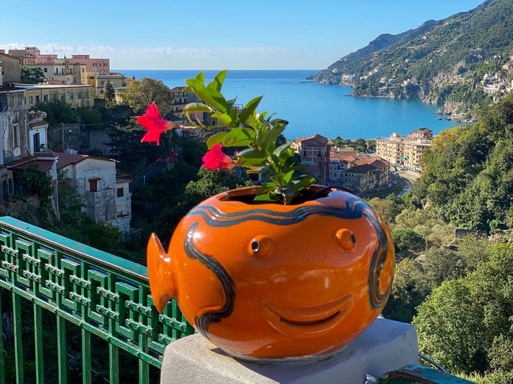 Cute orange fish-shaped flowerpot by a fence overlooking the buildings and beach of Vietri sul Mare
