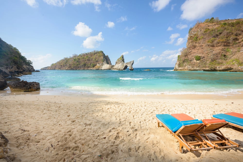 Atuh Beach on Nusa Penida with several deck chairs and a cloudy, blue sky