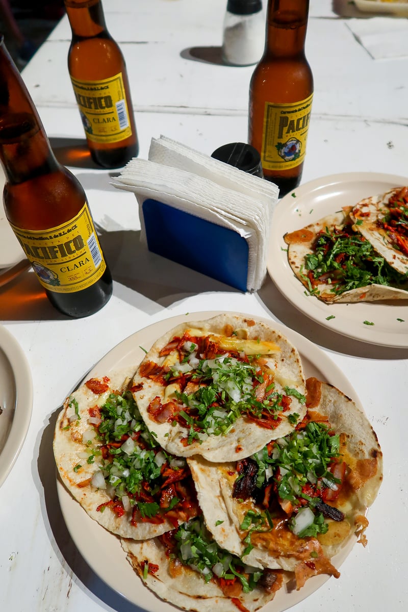 Tacos al pastor served on a plate and some bottles of beer