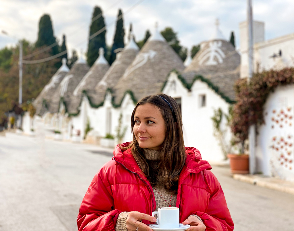 Melanie holding a cup of hot beverage while roaming the streets of Alberobello. If you're wondering where to go in Puglia, Italy, Alberobello is known for its trulli houses where you can try to stay in during your visit.
