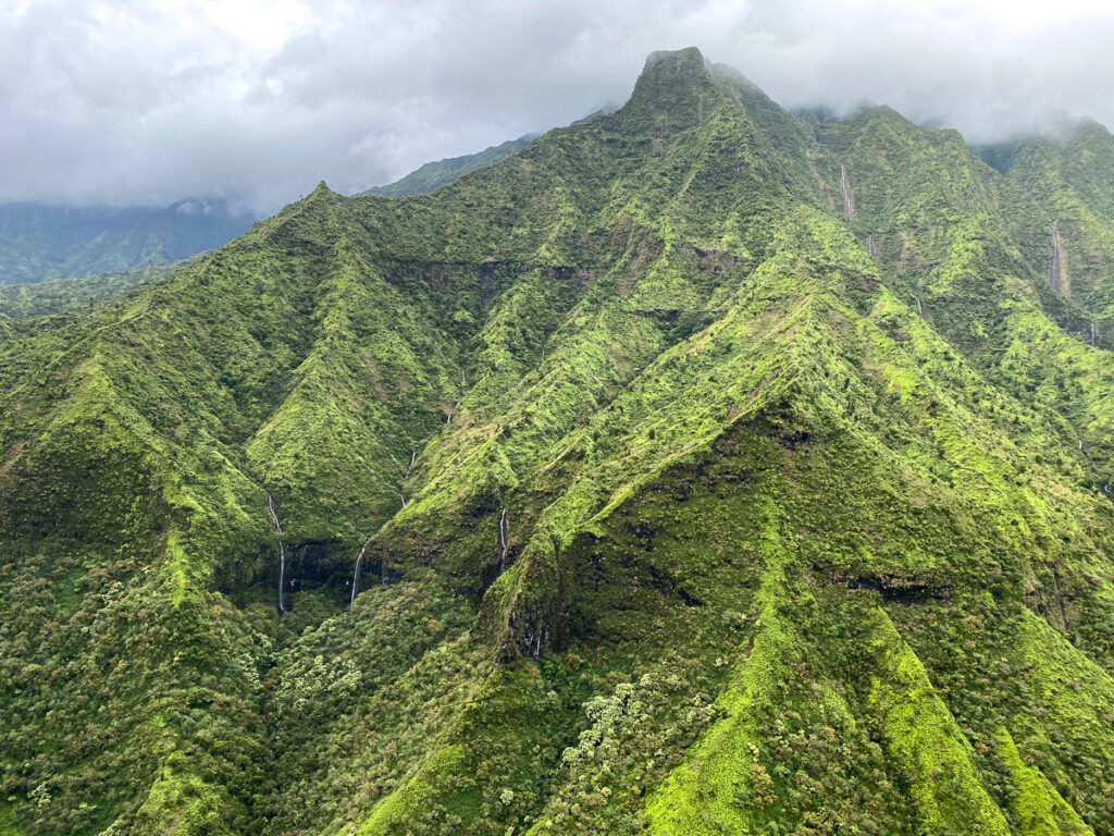 Lush green mountains in Kauai reaching out the fogs above them.