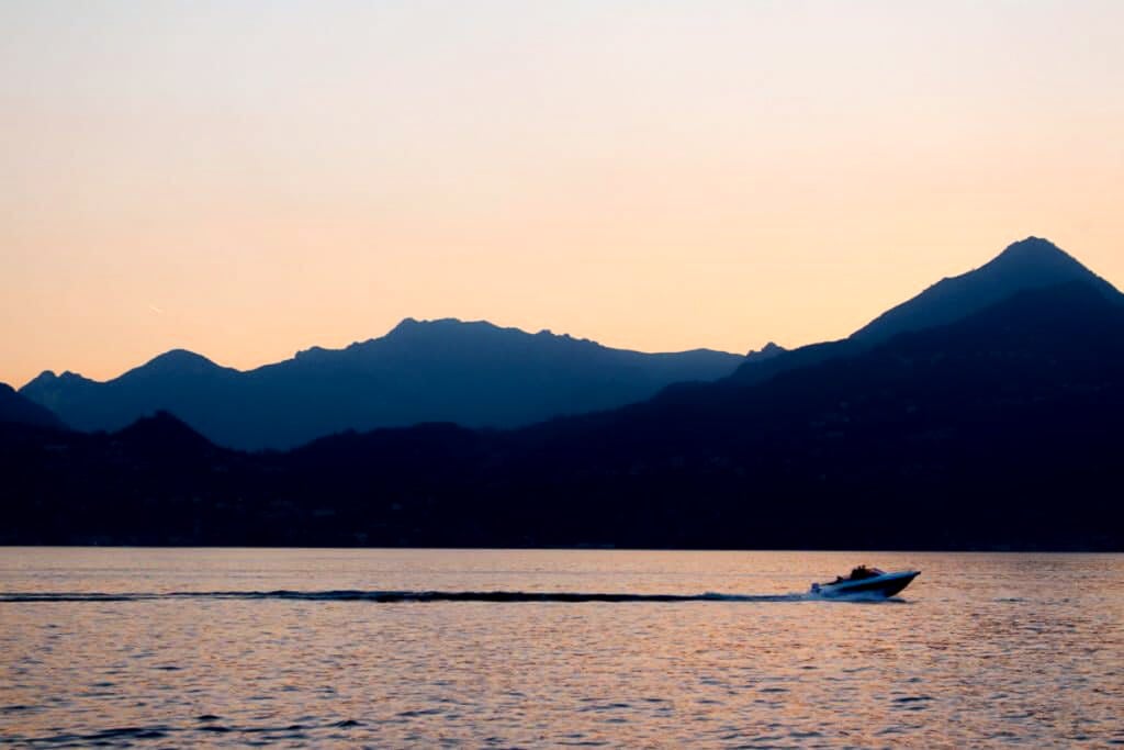 The sun setting over the mountains on Lake Como as a boat floats by.