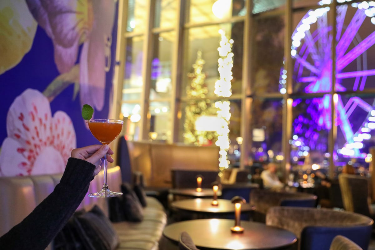 Raising a glass of cocktail at Blue Fox The Bar with a view of the Ferris wheel glowing at night