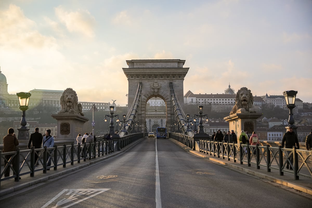 The Chain Bridge in Budapest with two lion statues on both sides with people and vehicles passing by