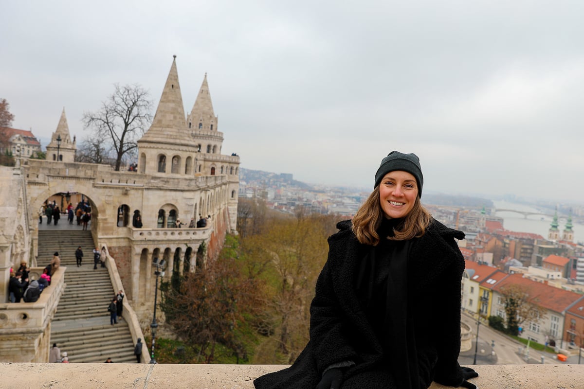 Maddy sitting on a stone fence with the Fisherman's Bastion behind her