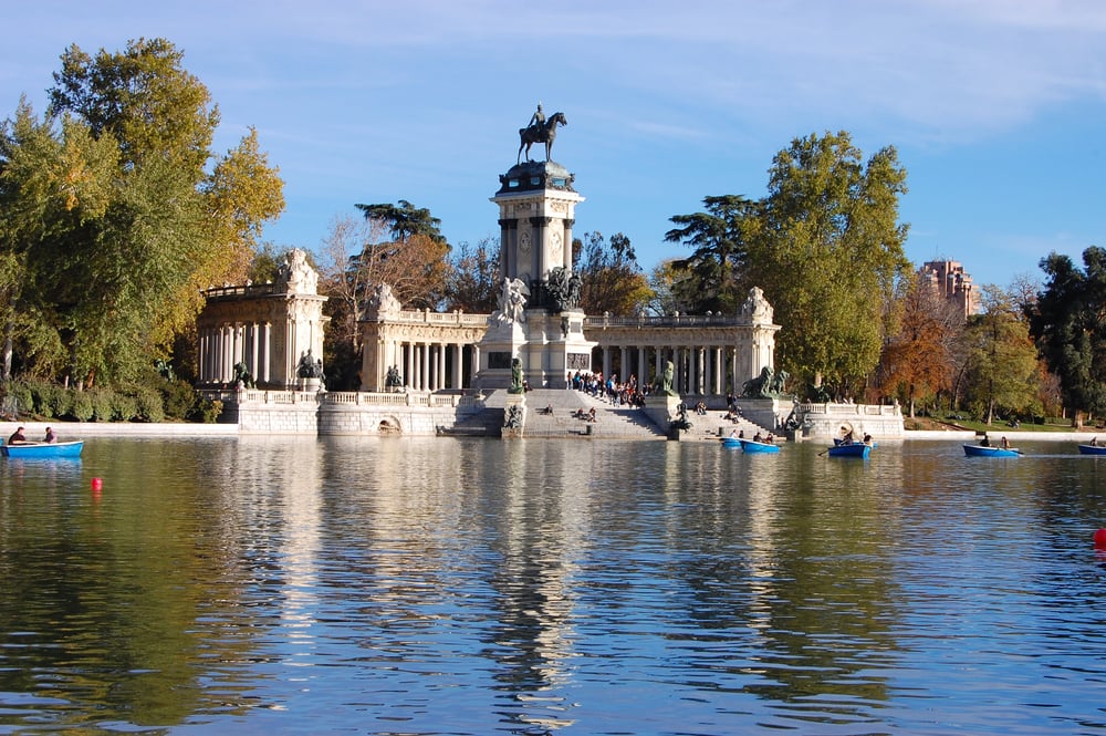 People boating in the lake of El Retiro Park as a monument of a knight stands tall