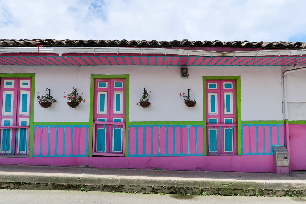 Colorful houses in Salento painted in pink, blue, and green on its doors, walls, and ceilings. Beautiful potted plants also hang by the doors.