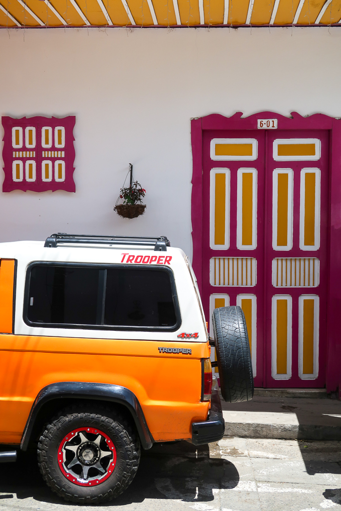 A white and orange car parked in front of a colorful door in Calle Real in Salento, Colombia