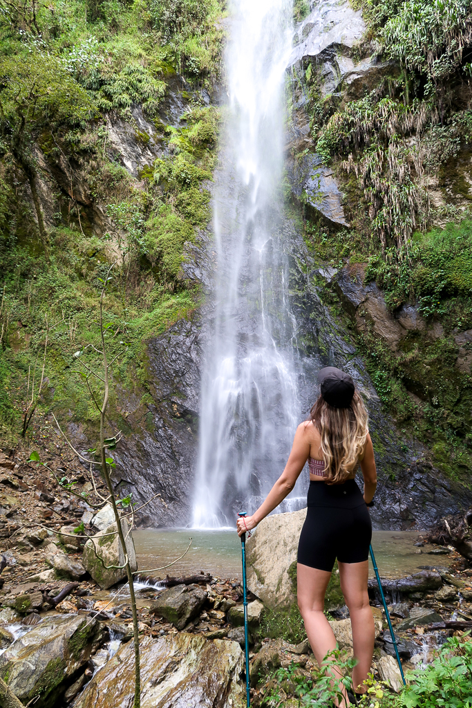 Maddy staring up the top of a waterfall in Cocora Valley with trekking poles in her hands