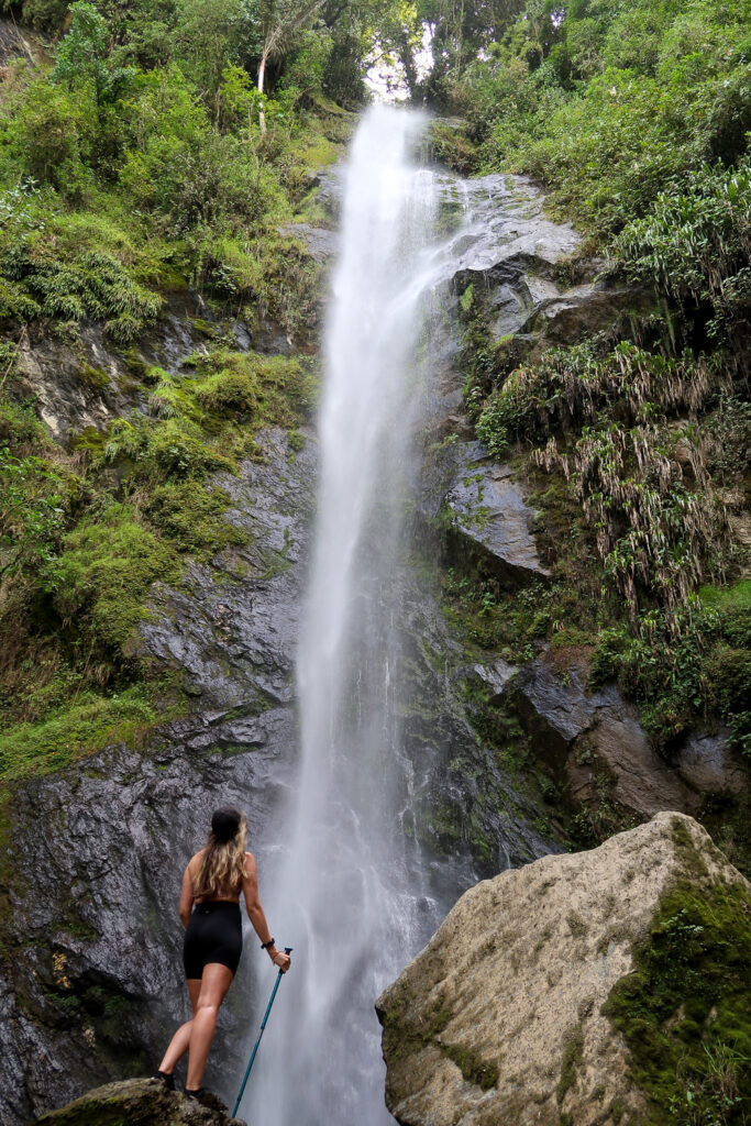 Maddy gazing at the top of a waterfall in Cocora Valley while standing on a big rock