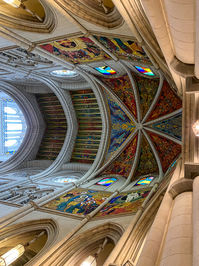 View of Almudena Cathedral's dome ceiling with various paintings of non-traditional and religious designs