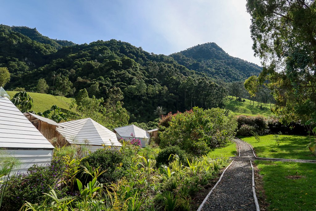 White-painted wooden tent-cabins near the lush mountains in Salento. Glamping in the nature is one of the things to do in Salento, Colombia that you should not miss!