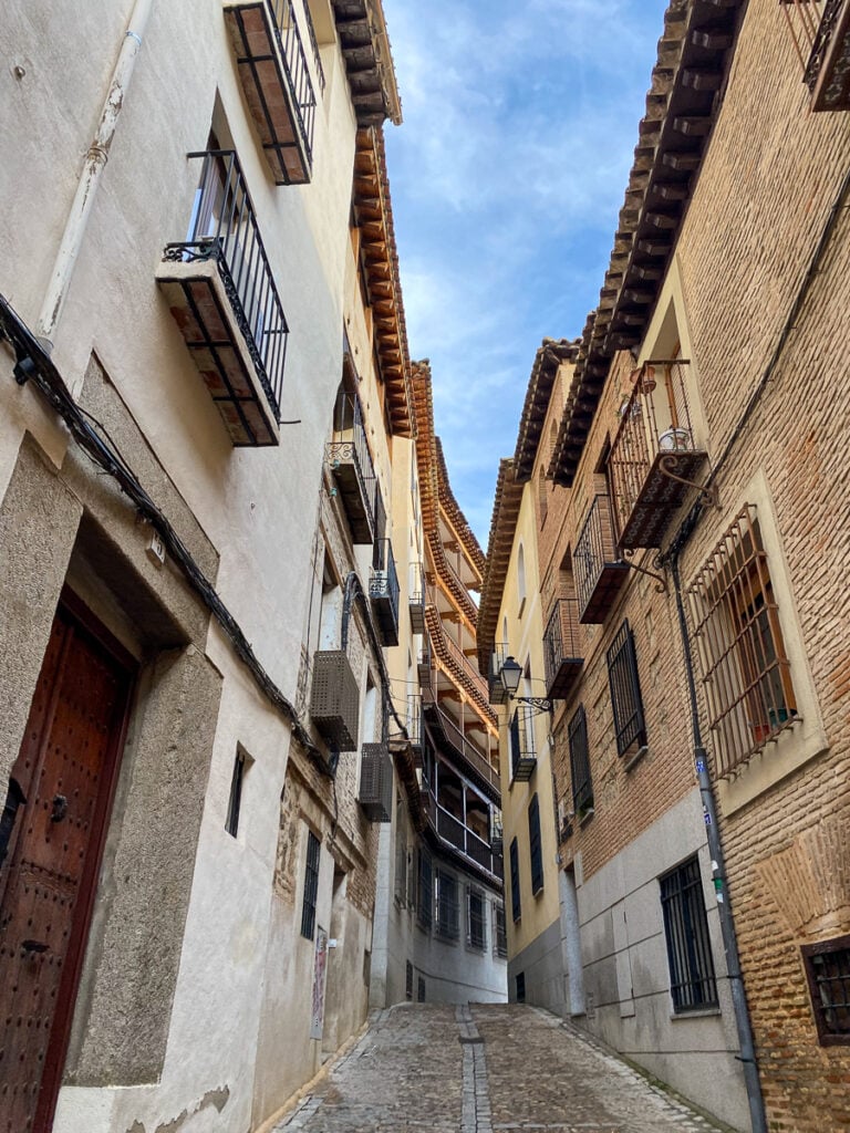 A narrow cobblestone street in the city of Toledo surrounded by tall medieval-designed buildings during daytime