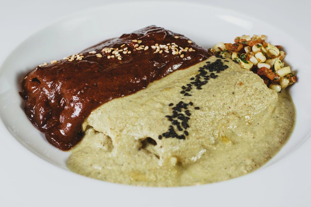 Two types of Mexican mole - mole negro and pipian - covering enchiladas on a white plate