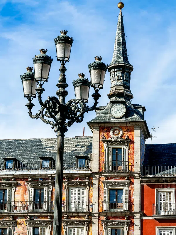 A tall lamp post in front of a building with beautiful architecture in Plaza Mayor