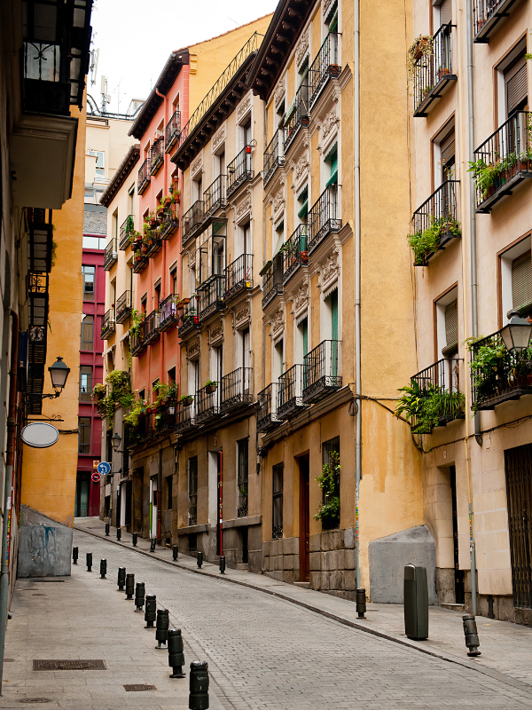 Narrow street walkway between tall, yellow-painted apartment buildings in Madrid