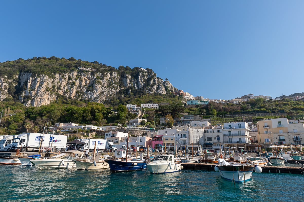 The colorful harbor of the island of Capri with boats in the water and the mountainous landscape in the background