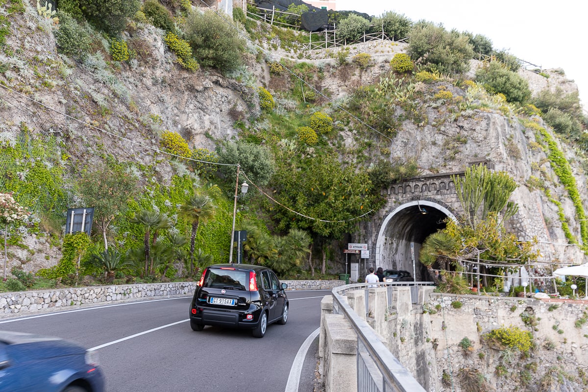 Cars driving down the narrow and winding Amalfi Coast Drive as pedestrians walk by carefully