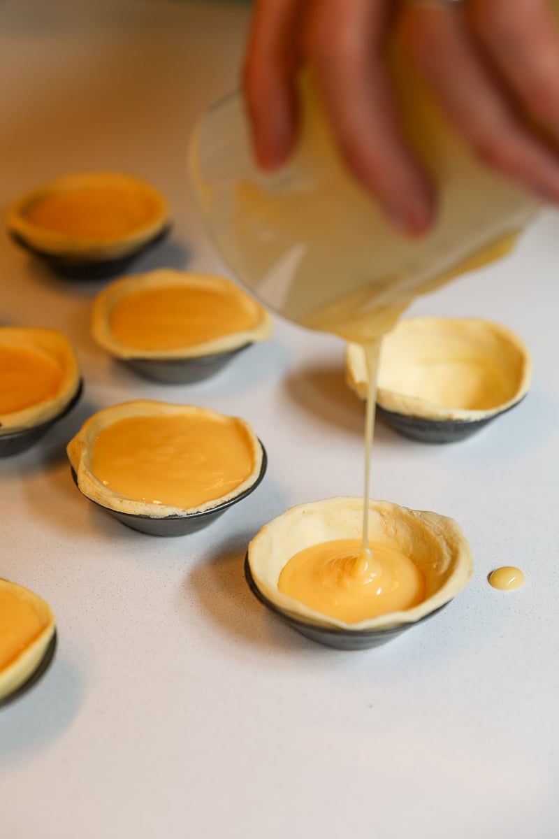 Pouring the creamy custard filling into the flaky pastry shell of pastel de nata during our Portuguese cooking class