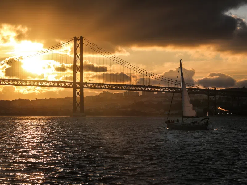 Sailboat sailing on the Tagus river under the April 25 Bridge at sunset