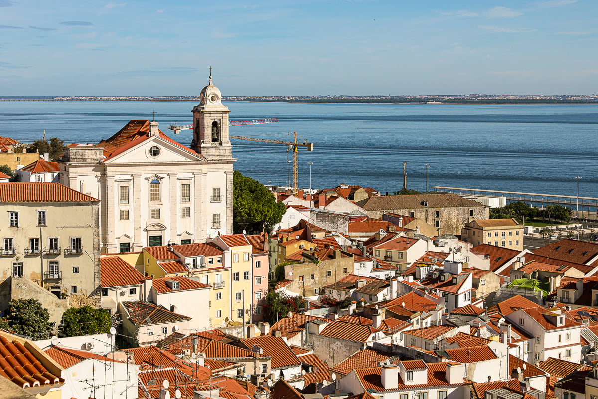 Church in Alfama, Lisbon towering over the red rooftops with a view of the sea in the background