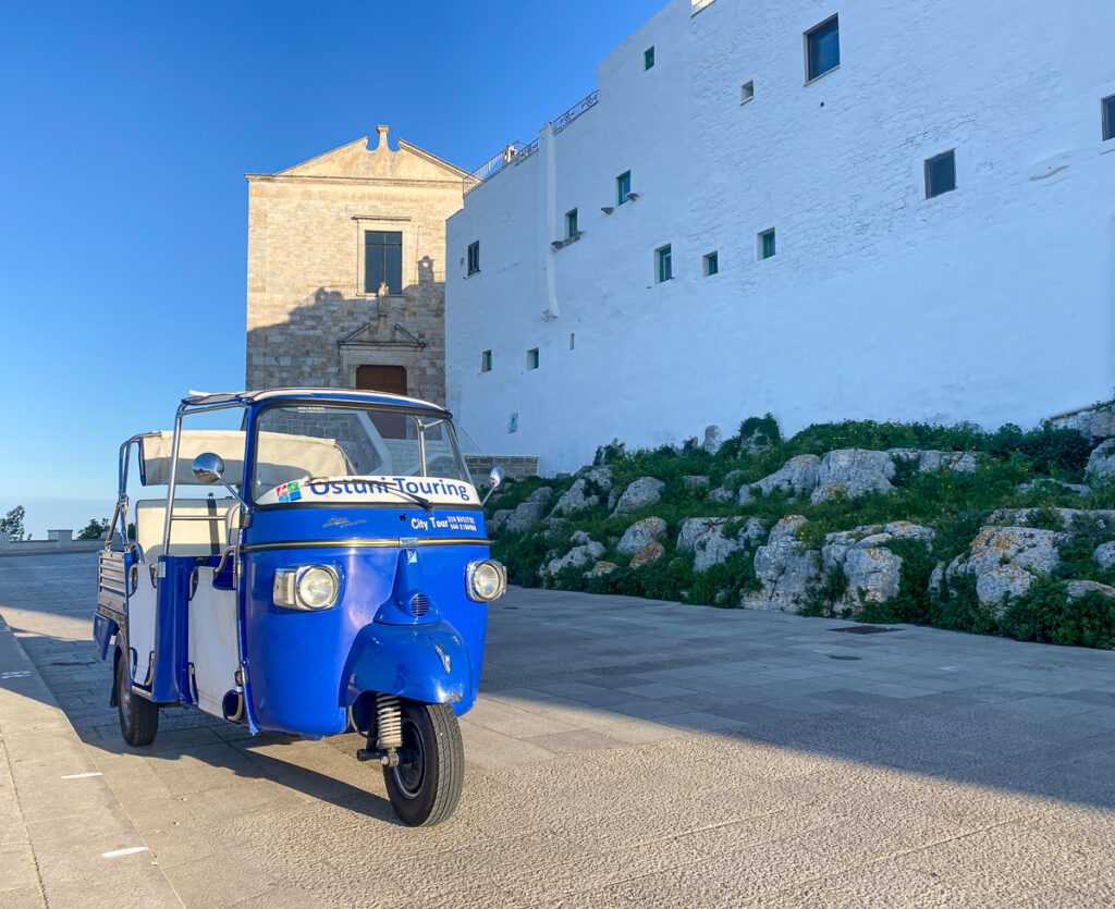 Vintage tuk-tuk near a white building in Ostuni. Wondering why visit Puglia? You can explore the towns and learn about Italian culture while riding a tuk-tuk.