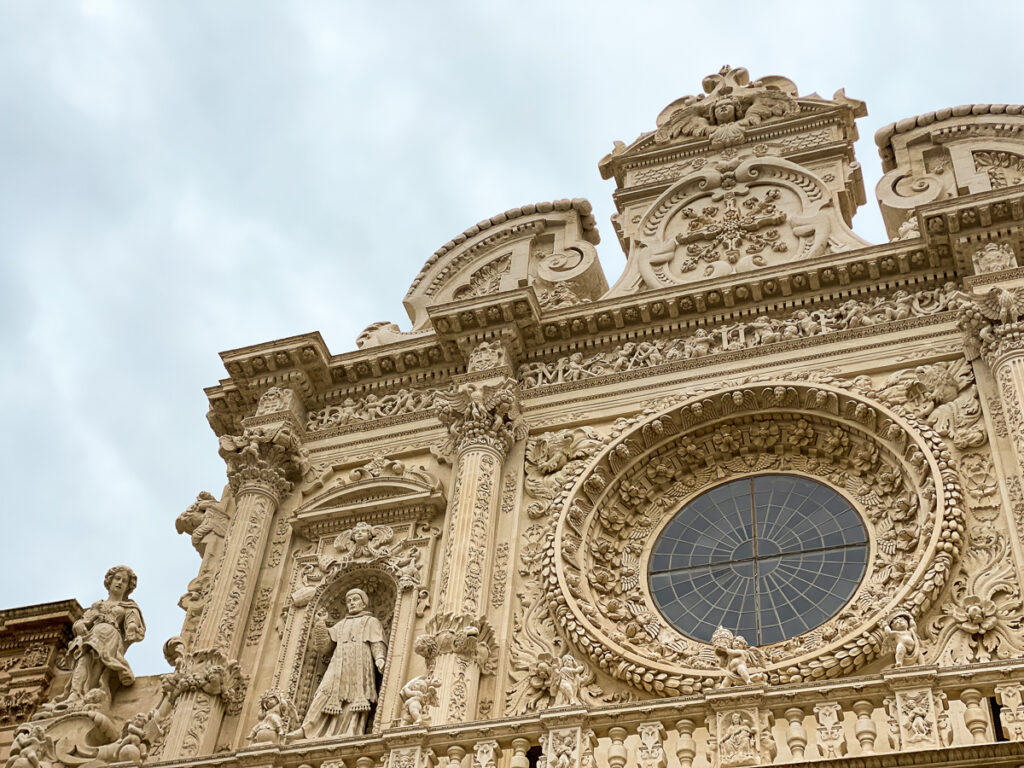 The central rose window surrounded by ornate architecture and stone carvings. The Basilica di Santa Croce is a must-see in Lecce, Italy.