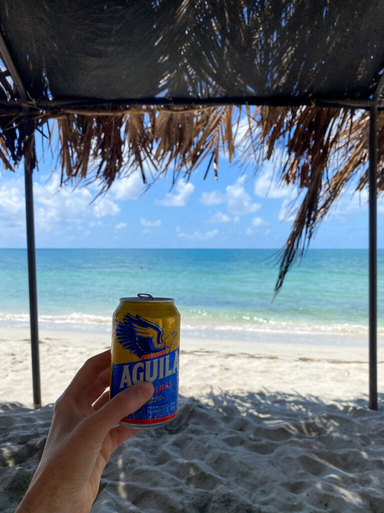 Holding up a can of beer while hanging out on the white-sand beach. Lounging at Almond Bay is one of the top things to do in Providencia, Colombia.