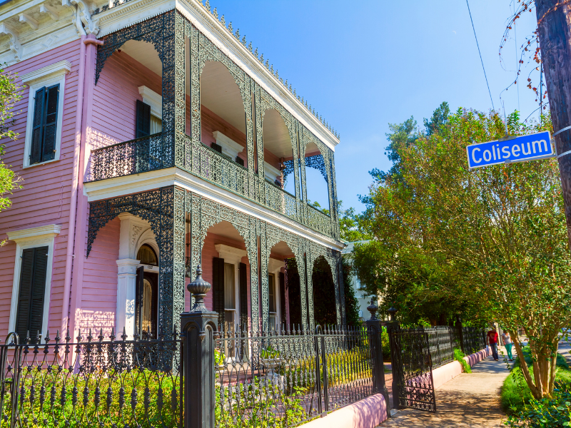 A beautiful pink house with wrought iron details surrounded by trees in the Garden District