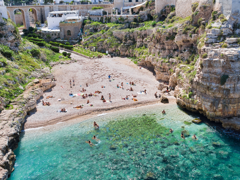 Crowd of people relaxing and hanging out by a small beach in Polignano a Mare