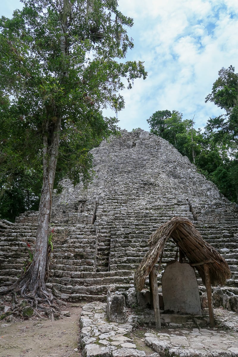 A very tall Maya pyramid with a stone slab with ancient inscriptions on it in the foreground