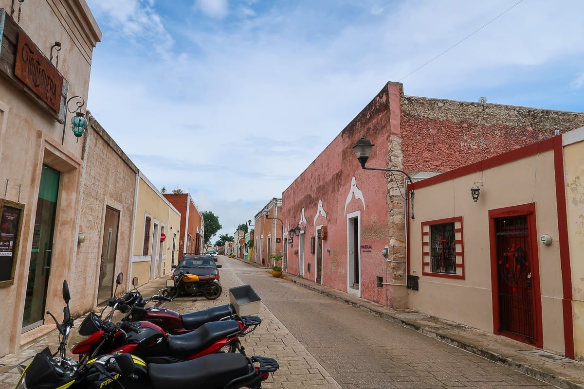 A colorful street in Valladolid with many scooters parked along the side