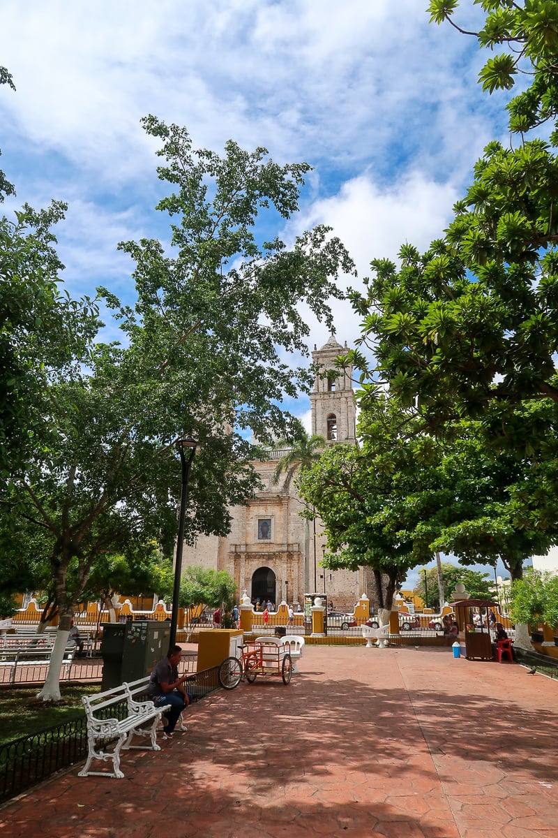 The leafy central plaza in Valladolid, with the church in the background and a local man sitting and eating an ice cream cone in the foreground