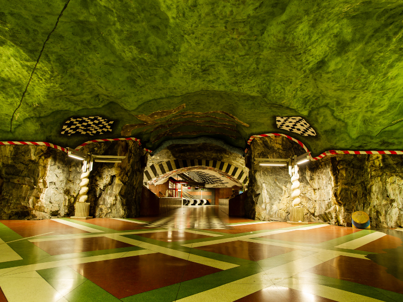 A metro station in Stockholm with beautiful floor tile and exposed rock walls and ceiling adorned in lovely art