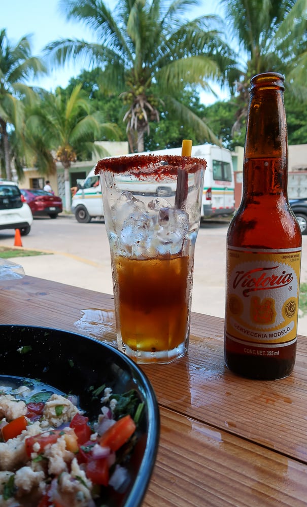 Ceviche, a glass of michelada, and a bottle of beer at a Yucatan restaurant. Wondering what to do in Sisal? Eating delicious seafood served with micheladas is a must-try!