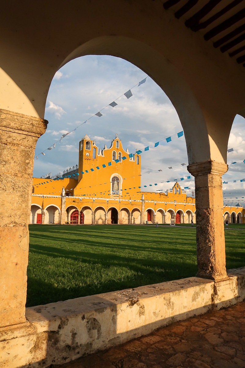 Yellow convent in Izamal seen through an archway. Looking for tips while traveling the Yellow City? This guide covers the essentials.
