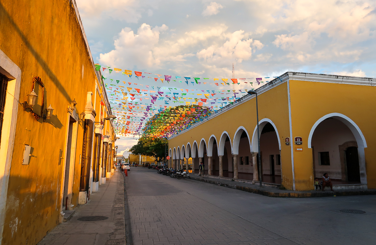 Colorful festive flags hanging between the yellow buildings in Izamal
