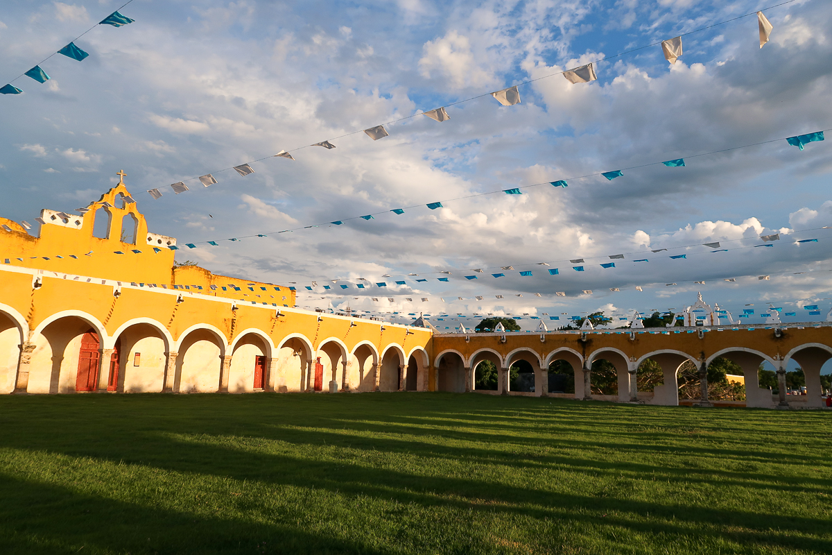 Yellow convent in Izamal decorated with colorful flags. Find more tips for your Izamal travel in this guide.