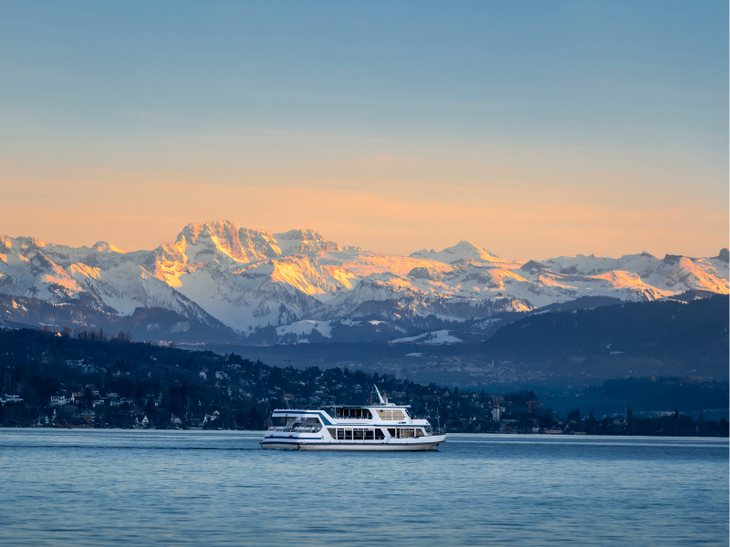 Snow-capped mountains and orange skies, and a boat, at Lake Zurich