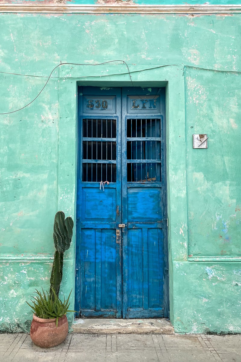 A house in Merida with green walls and a potted cactus by its blue wooden door