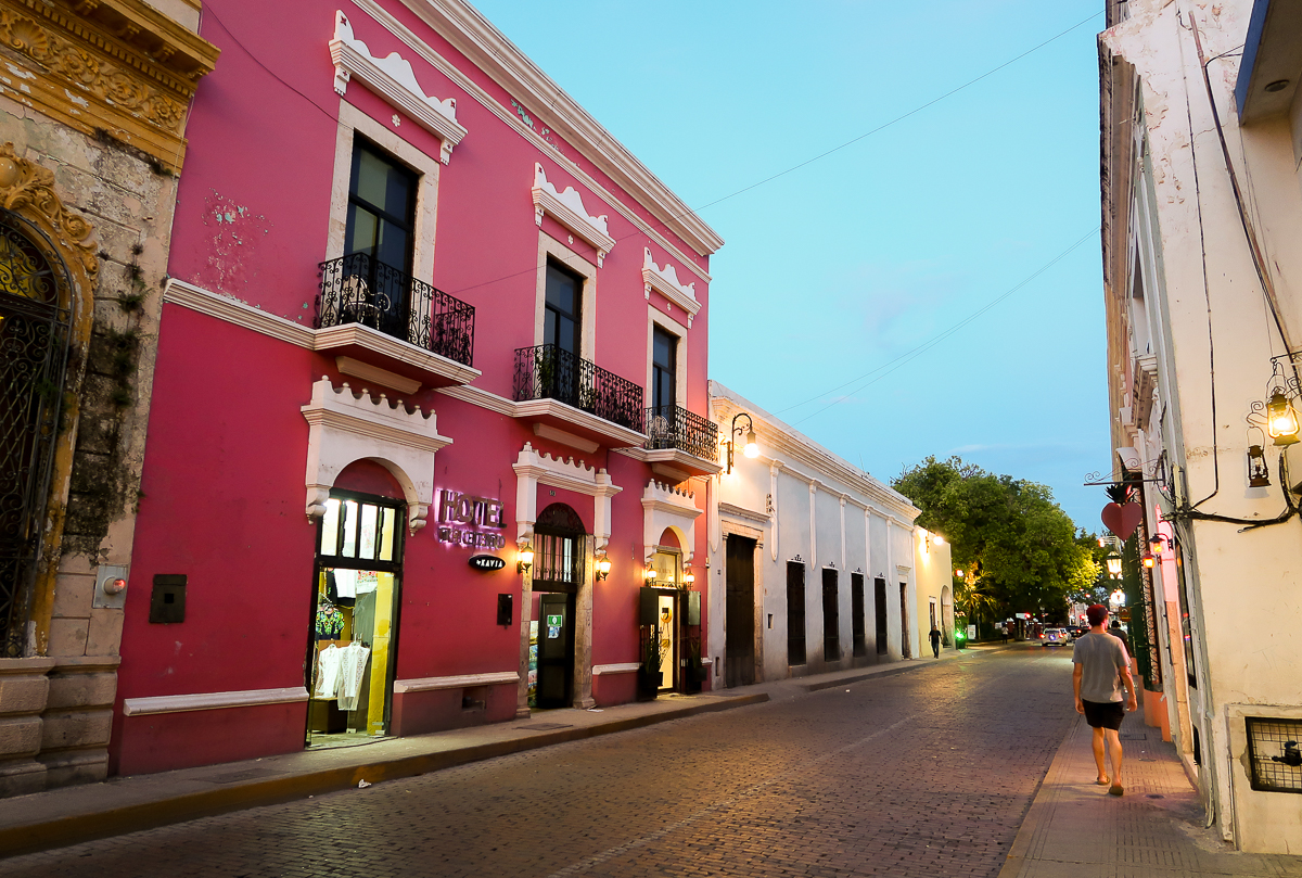 Colorful buildings along the street of Merida with lit outdoor lamps at dusk