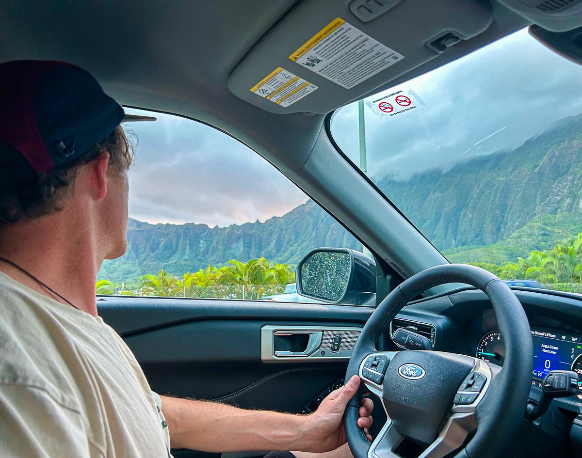 Cacey driving while enjoying the beauty of the mountains. Don't forget to book a rental car to enjoy your road trip to the North Shore.