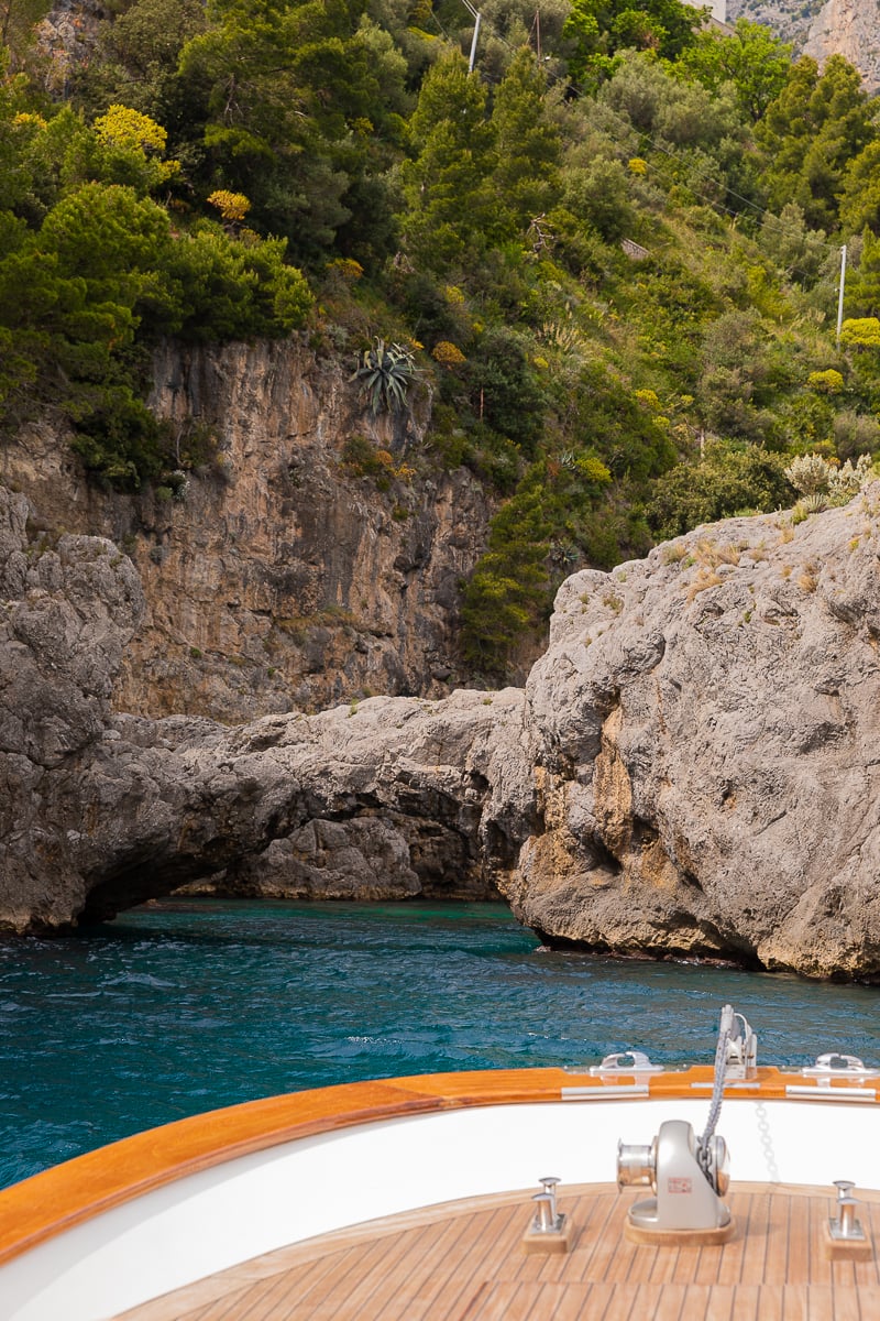 A wooden boat in the sea with a rock arch in the background