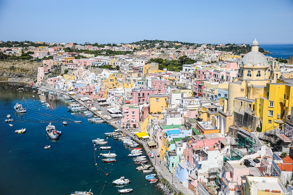 Colorful, vibrant buildings in Procida, Italy with boats docked along the waters on a sunny day